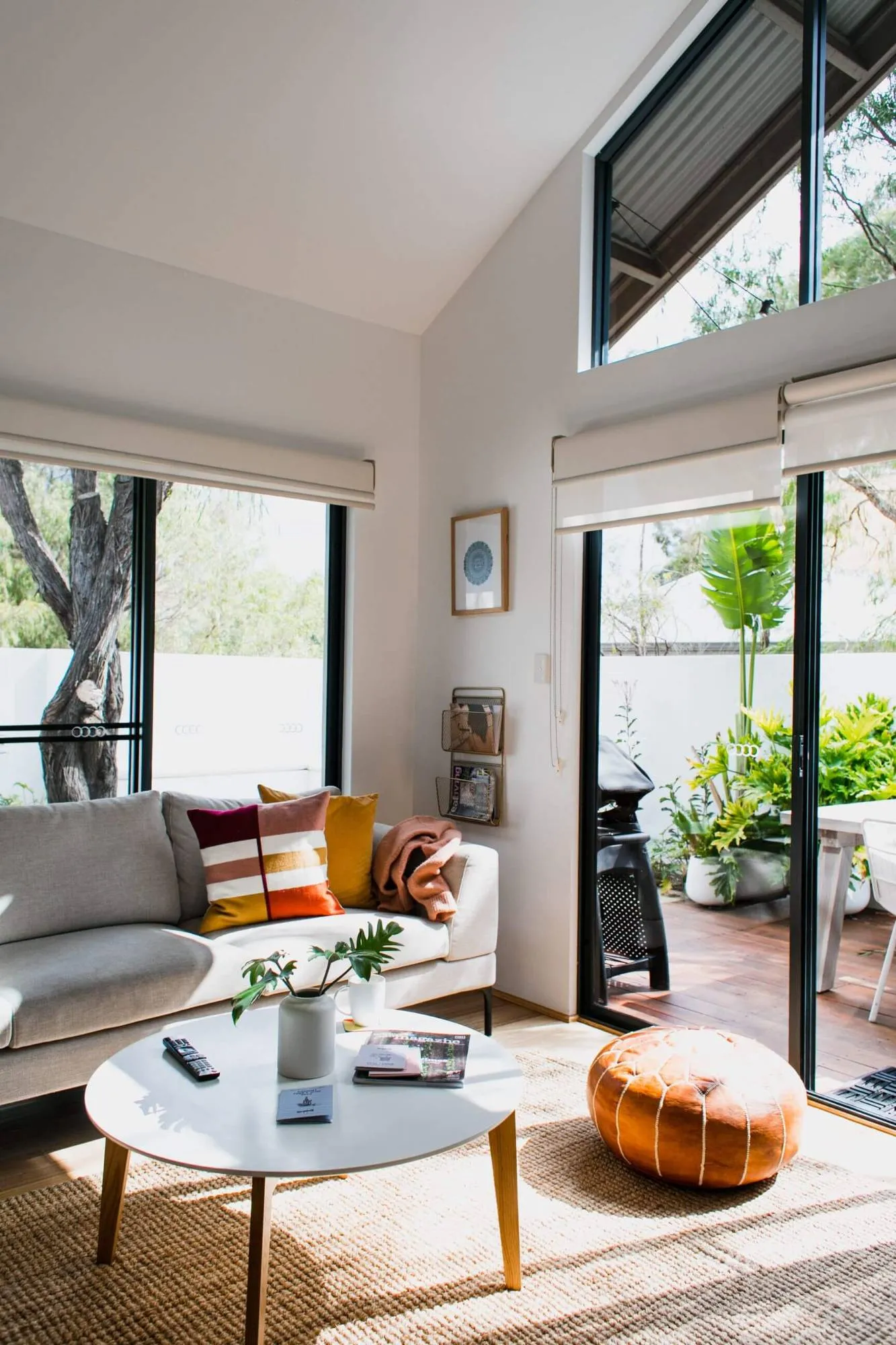 Sunlit living room with a light grey sofa, round coffee table and leather pouf