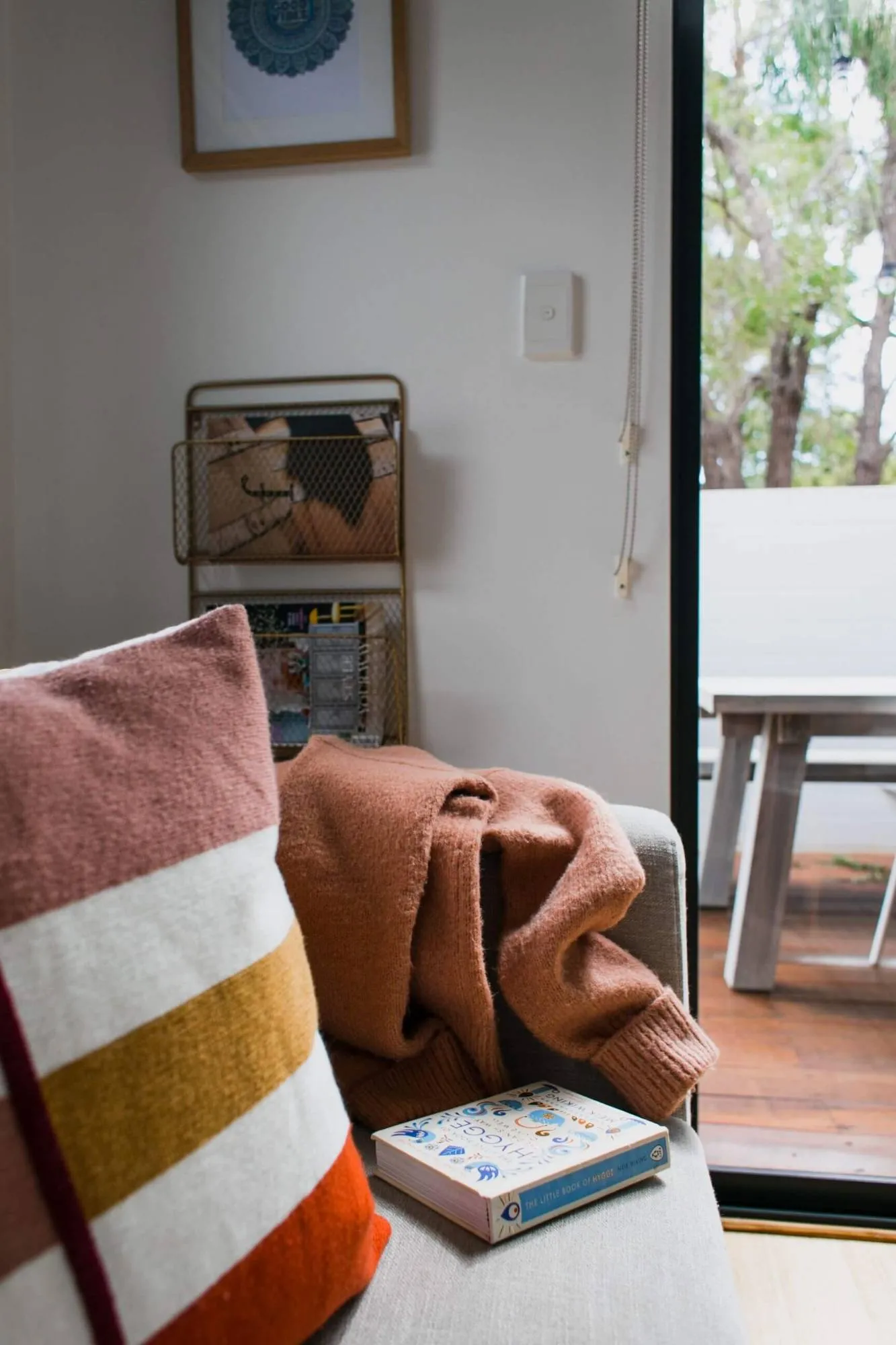 Cushion, knitted throw and a book resting on a clean linen sofa